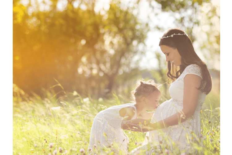 Kobieta w ciąży i mała dziewczynka bawią się na łące w białych sukienkach – Sesja zdjęciowa plenerowa
