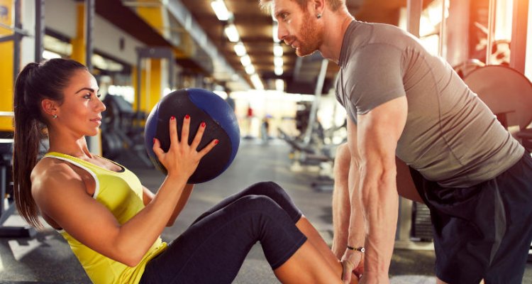 Trener personalny ćwiczy z podopieczną przy pomocy dużej piłki
