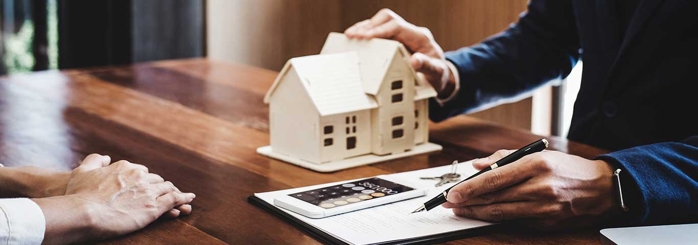doradca kredytowy wyjaśnia klientowi warunki kredytu hipotecznego trzymając w jednej ręce długopis a w drugiej mały domek