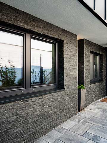 front domu z nowoczesną elewacją z kamienia i oknami z czarnymi framugami
