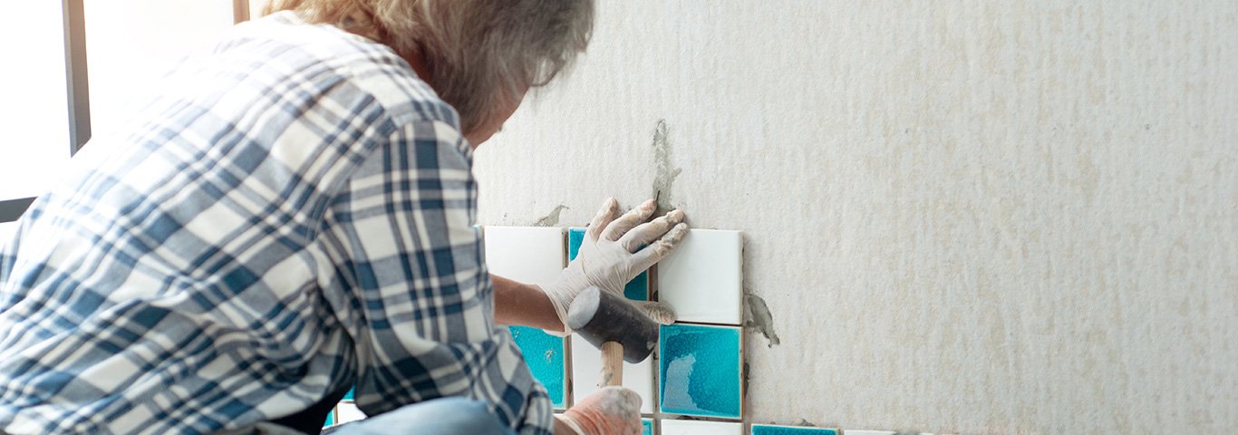 glazurnik dobija młotkiem gumowym kolorowe płytki ułożone na ścianie