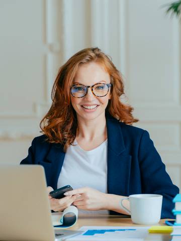 uśmiechnięta rudowłosa kobieta siedzi przy biurku i pracuje przy laptopie