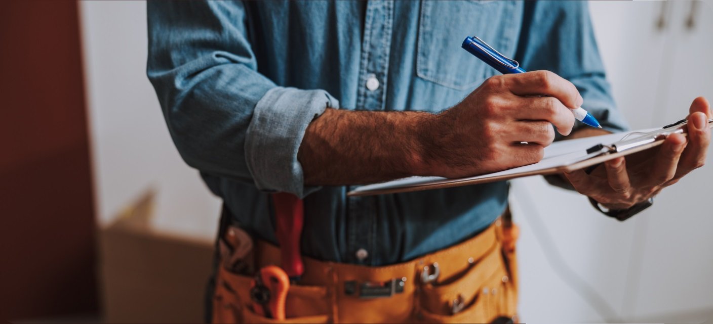 Zbliżenie na piszącego pracownika budowlany ubranego w dżinsową koszulę i pas narzędziowy.